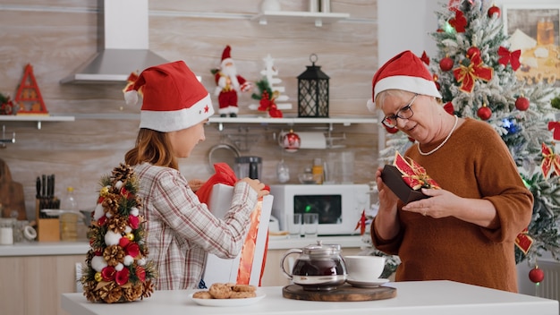 Familia feliz vistiendo gorro de Papá Noel sorprendiéndose unos a otros con envoltorio regalo de Navidad presente