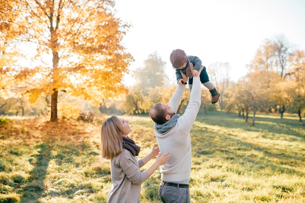 Família feliz vomitar seu bebê adorável no ensolarado parque outono.