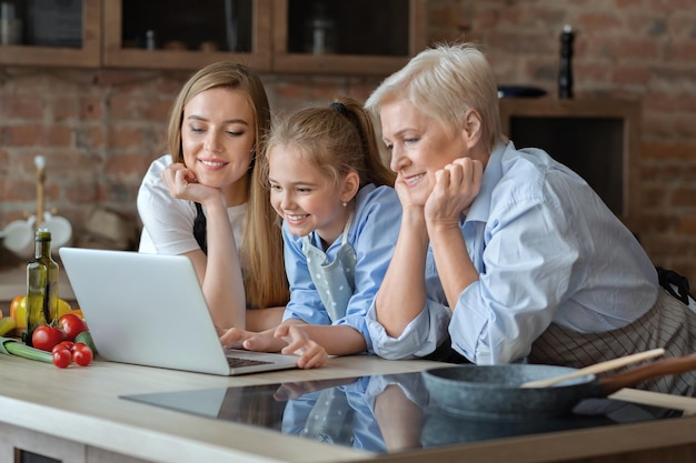 Família feminina feliz procurando receita na internet, usando o laptop na cozinha, espaço livre