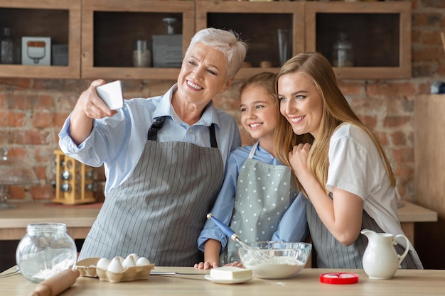 Família feminina feliz tomando selfie no smartphone enquanto assava na cozinha, copie o espaço