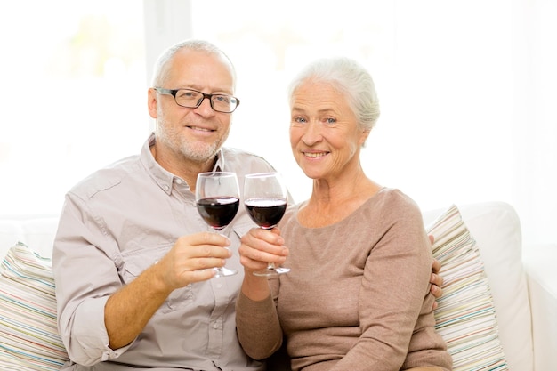 família, feriados, bebidas, idade e conceito de pessoas - casal sênior feliz com copos de vinho tinto em casa