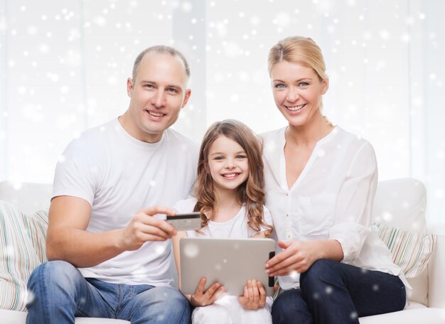 família, feriados, compras, tecnologia e conceito de pessoas - família feliz com computador tablet pc e cartão de crédito sobre fundo de flocos de neve