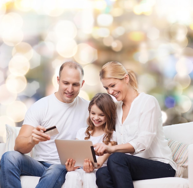 família, feriados, compras, tecnologia e pessoas - sorrindo, mãe, pai e filha com computador tablet pc e cartão de crédito sobre fundo de luzes