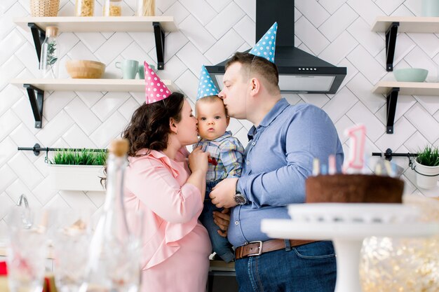 Família, feriados e conceito dos povos - mãe, pai e festa de aniversário pequena feliz do filho em casa, os pais estão beijando o bebê