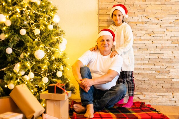 família, feriados, geração e conceito de pessoas - menina sorridente com o avô decorando a árvore de Natal em casa