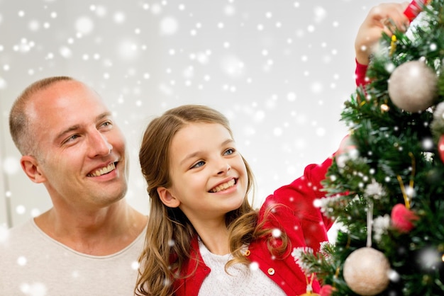 Família, feriados, geração e conceito de pessoas - menina sorridente com pai decorando a árvore de natal em casa