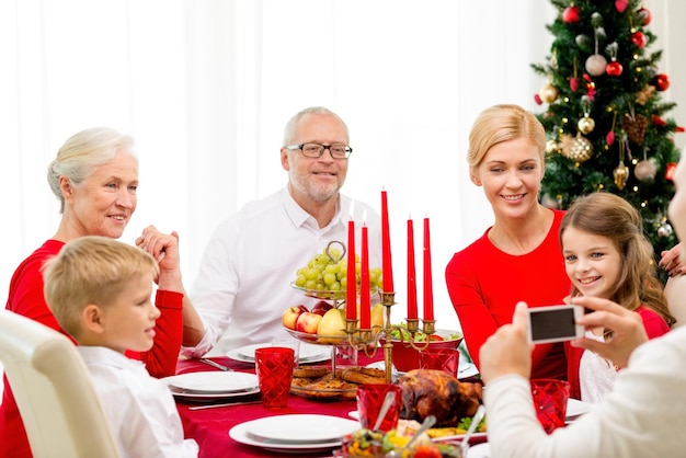 família, feriados, geração, natal e conceito de pessoas - família sorridente jantando e fazendo foto com câmera em casa