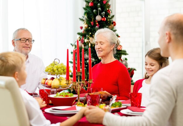 família, feriados, geração, natal e conceito de pessoas - família sorridente jantando e rezando em casa