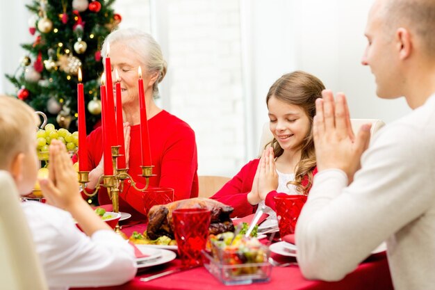 Foto família, feriados, geração, natal e conceito de pessoas - família sorridente jantando e rezando em casa