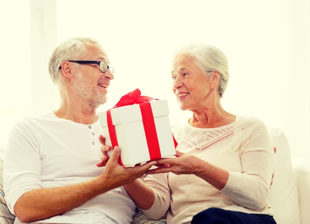 família, feriados, natal, idade e conceito de pessoas - casal sênior feliz com caixa de presente em casa