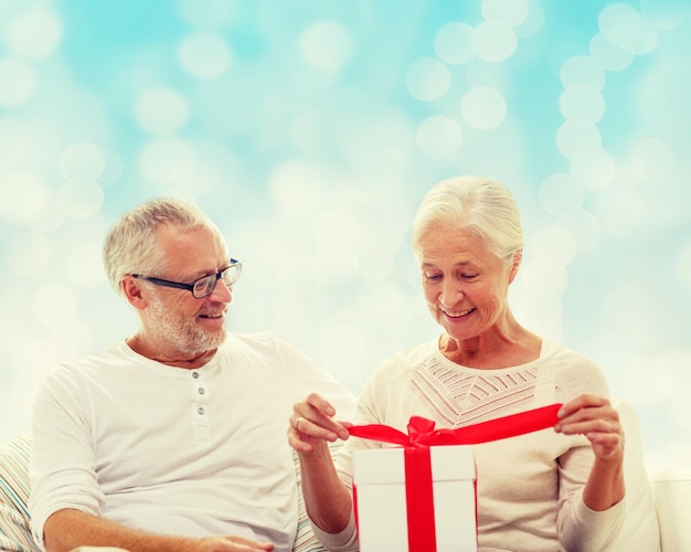 família, feriados, natal, idade e conceito de pessoas - casal sênior feliz com caixa de presente sobre fundo de luzes azuis