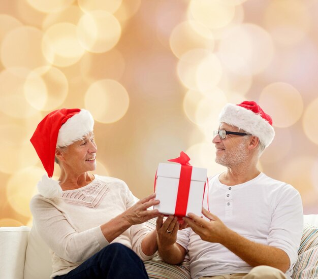 família, feriados, natal, idade e conceito de pessoas - casal sênior feliz em chapéus de ajudante de papai noel com caixa de presente sobre fundo bege