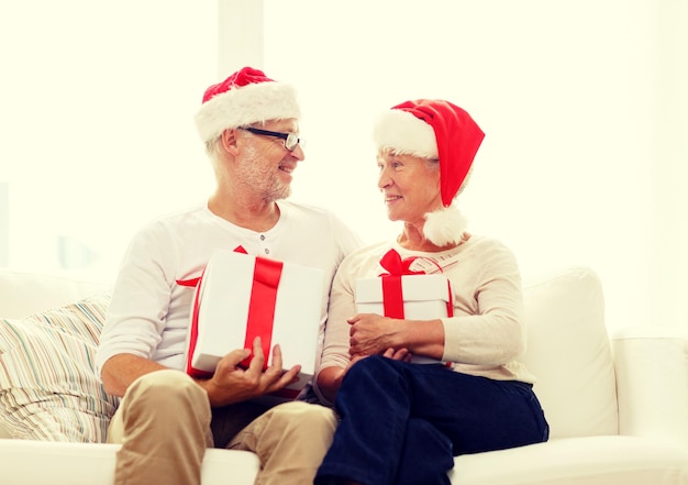 família, feriados, natal, idade e conceito de pessoas - casal sênior feliz em chapéus de ajudante de papai noel com caixas de presente em casa