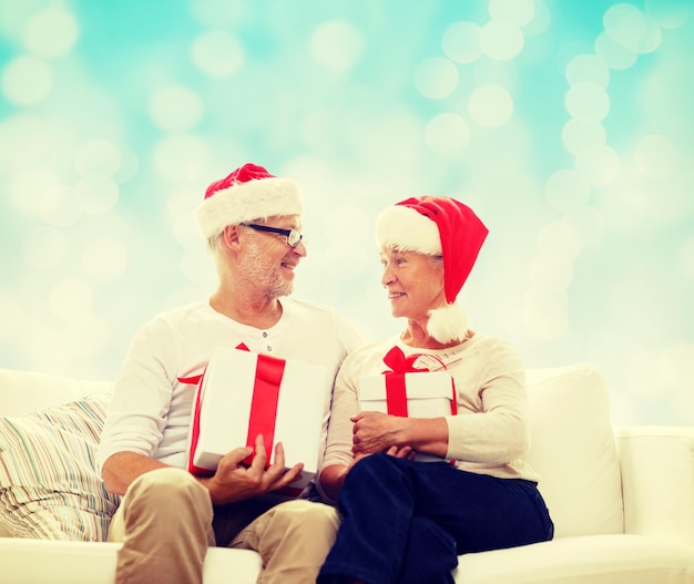 família, feriados, natal, idade e conceito de pessoas - casal sênior feliz em chapéus de ajudante de papai noel com caixas de presente sobre fundo de luzes azuis