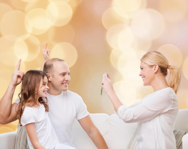 família, feriados, tecnologia e conceito de pessoas - sorrindo mãe, pai e filha com câmera sobre fundo de luzes bege