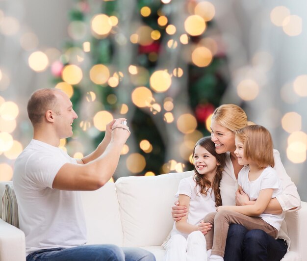 família, feriados, tecnologia e pessoas - sorrindo mãe, pai e filhas com câmera sobre fundo de luzes da árvore de natal