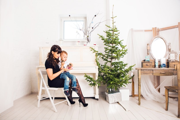 Família, férias e conceito de Natal - mãe e filho perto da árvore de Natal