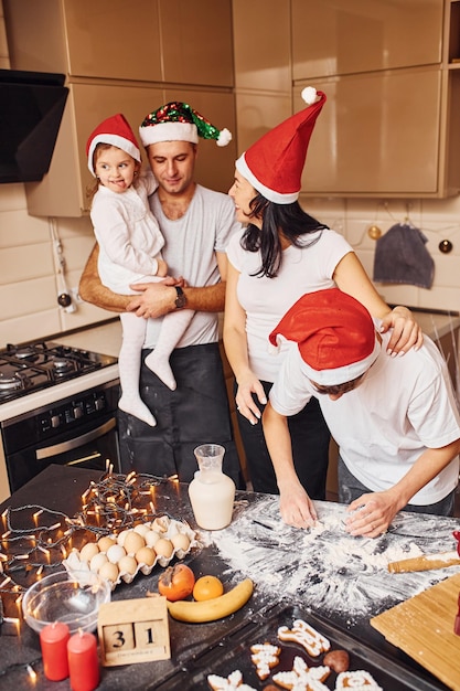 Família festiva em chapéus de natal se diverte na cozinha e preparando comida.