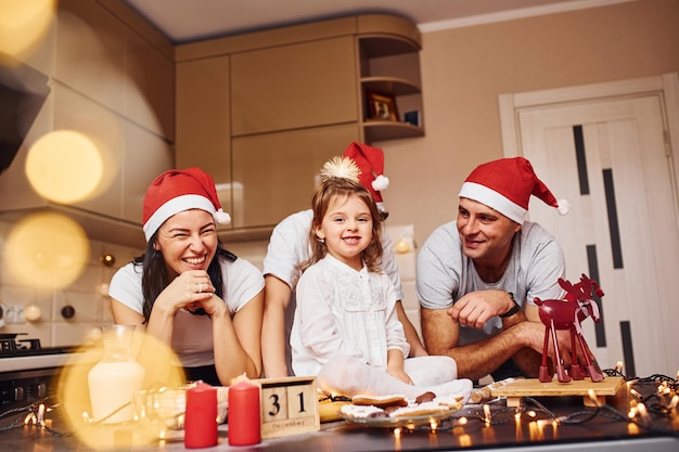 Família festiva em chapéus de natal se diverte na cozinha e preparando comida.