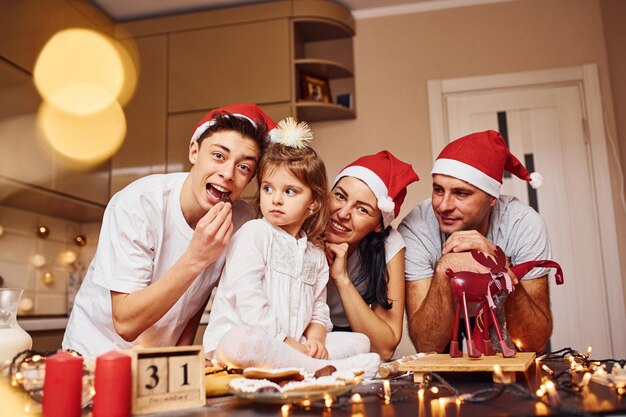 Família festiva em chapéus de natal se diverte na cozinha e preparando comida.