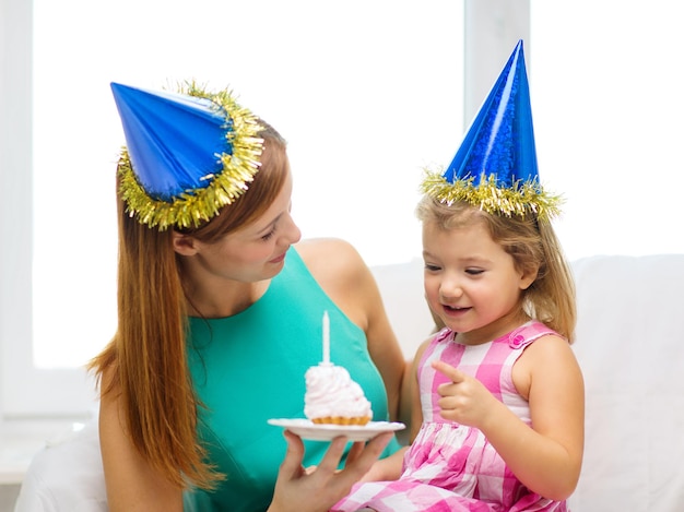 família, filhos, celebração e conceito de pessoas felizes - mãe e filha felizes em chapéus de festa azuis com bolo e vela