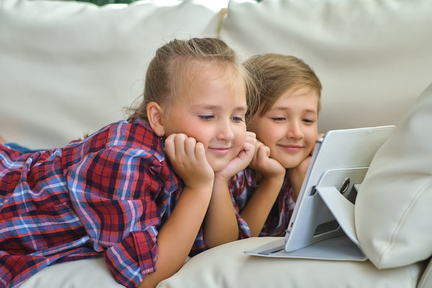 Família, filhos, tecnologia e conceito de casa - irmão e irmã sorrindo com o computador tablet pc no sofá da sala de estar