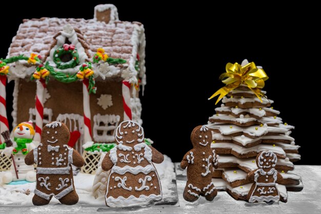Família fofa de gengibre perto da casa de pão de mel caseiro coberta de neve e árvore de natal. maquete para ofertas sazonais e cartão postal de férias