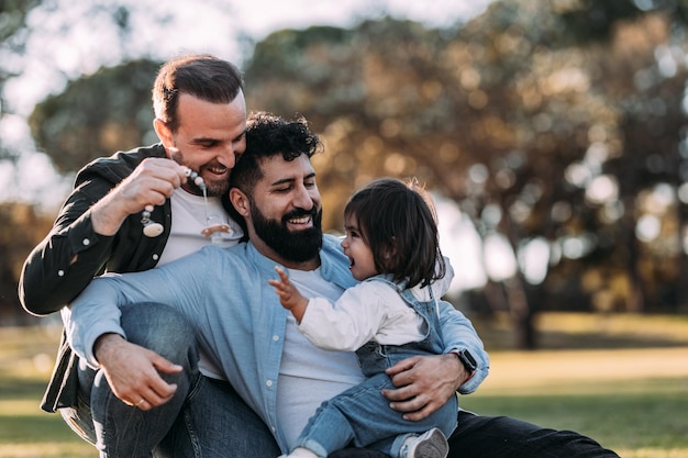 Familia gay masculina abrazando y jugando con su pequeña hija en el parque