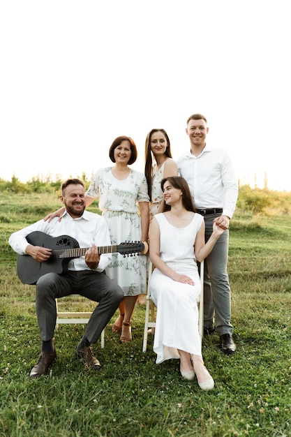 Una familia grande y hermosa con cinco personas riendo y hablando. retrato de familia al atardecer del día. el padre toca la guitarra para la familia. un grupo de personas de nacionalidad europea