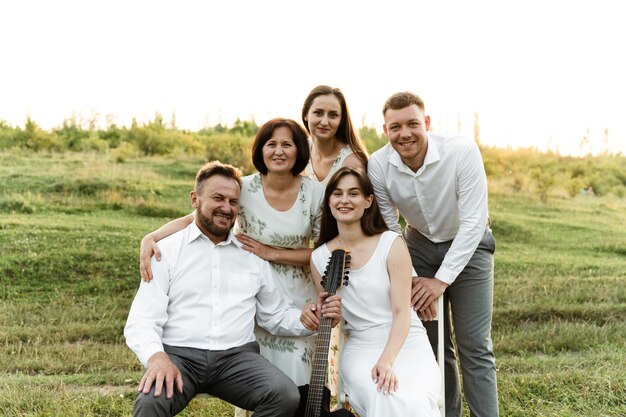 Una familia grande y hermosa con cinco personas riendo y hablando. retrato de familia al atardecer del día. el padre toca la guitarra para la familia. un grupo de personas de nacionalidad europea