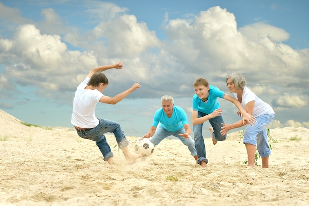 Família grande jogando futebol na praia em dia de verão