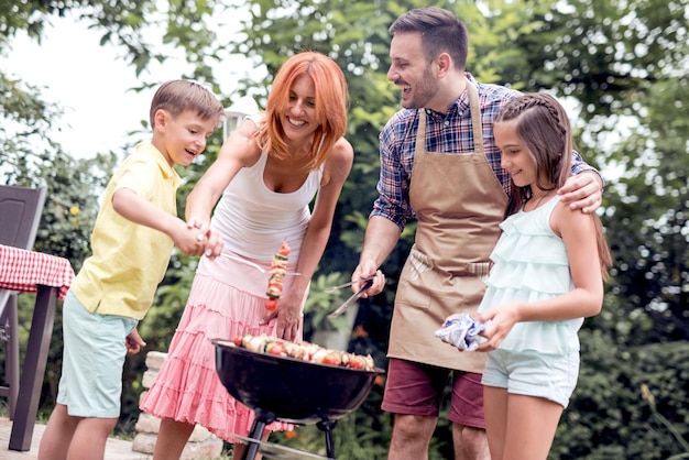 Foto familia haciendo una barbacoa de pie alrededor de la parrilla