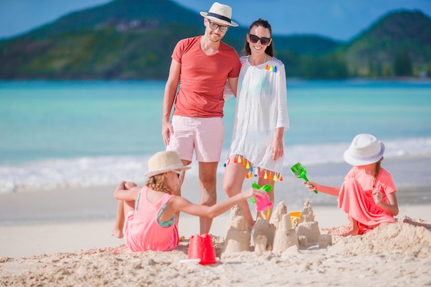 Familia haciendo castillos de arena en la playa blanca en vacaciones de verano