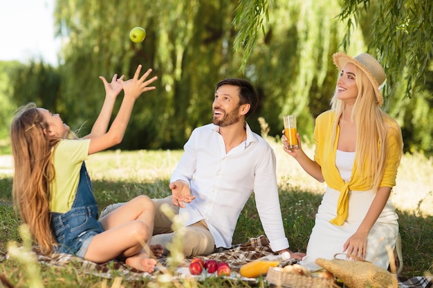 Familia haciendo picnic en la naturaleza niña haciendo malabares con manzana