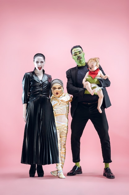 Familia de Halloween. Feliz padre, madre e hijos niñas en maquillaje y disfraz de Halloween. Tema sangriento: las caras del loco loco sobre fondo rosa de estudio