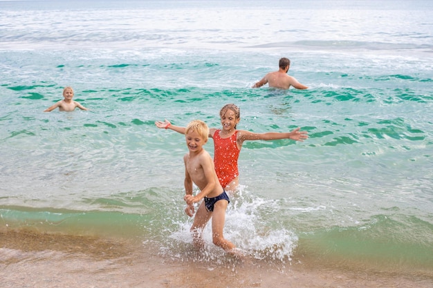 Una familia de hermanos y hermanas juegan y se divierten en el agua del mar y se ríen en un día de verano Vacaciones en el mar