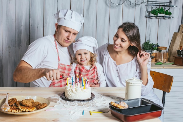 Foto familia, hija feliz con mamá y papá en casa en la cocina reír y encender las velas de la tarta de cumpleaños