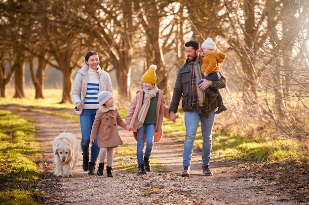 Familia con hija con síndrome de Down caminando con perro mascota en el campo de otoño o invierno juntos