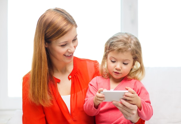 familia, hijos, paternidad, tecnología y concepto de internet - feliz madre e hija con smartphone en casa