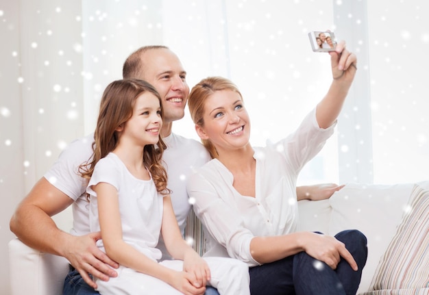 familia, hogar, tecnología y gente - familia feliz con cámara tomando fotos sobre fondo de copos de nieve