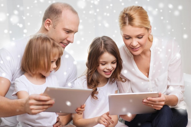 familia, hogar, tecnología y gente - madre, padre y niñas sonrientes con tabletas sobre fondo de copos de nieve