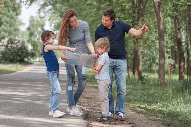 Familia con una hoja de ruta de pie al costado de la carretera.