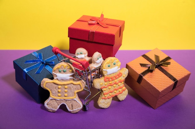 una familia de hombres de pan de jengibre con máscaras protectoras con un carrito de supermercado y regalos. orientación horizontal