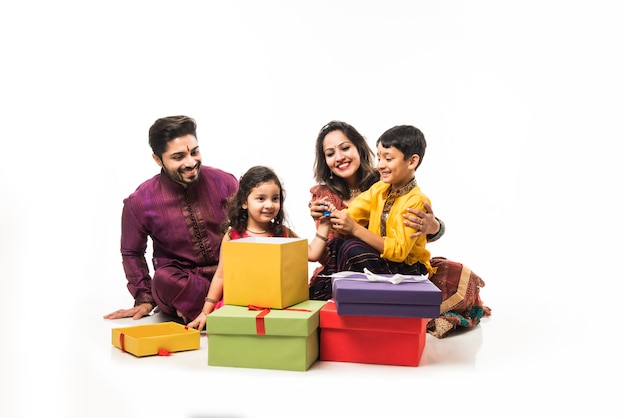 Familia india celebrando Diwali o Deepavali en ropa tradicional mientras está sentado aislado sobre fondo blanco con cajas de regalo y lámpara en thali