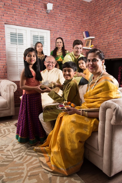 Familia india celebrando el festival Raksha Bandhan o Rakhi en casa mientras usa ropa tradicional y se sienta en el sofá