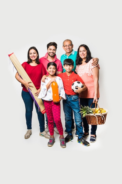 Familia india que va de picnic: varias generaciones de familias asiáticas de pie sobre un fondo blanco con canasta de frutas, tapete, fútbol y bebidas. enfoque selectivo