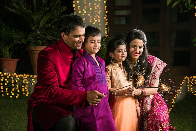 Familia india en ropa tradicional jugando con bengalas o phuljhadi mientras celebra el festival de diwali, al aire libre