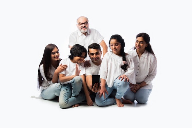 Familia india de seis videollamadas en el teléfono inteligente o tomar una foto selfie contra un blanco