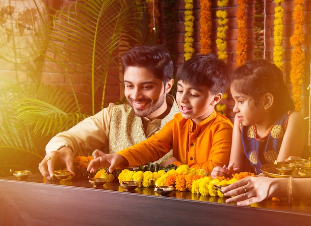 Família indiana acendendo ou arranjando lamparina a óleo ou diya em torno de rangoli de flores na noite do festival de Diwali