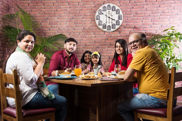 Família indiana comendo comida na mesa de jantar em casa ou restaurante fazendo as refeições juntos